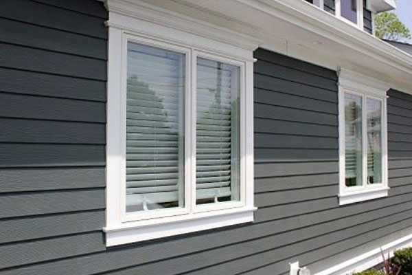 Close-up of a house exterior with gray siding and white-trimmed windows.