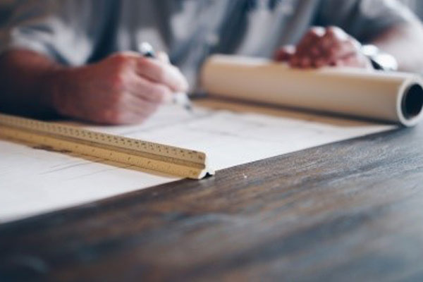 A person's hands drawing on architectural plans with a ruler