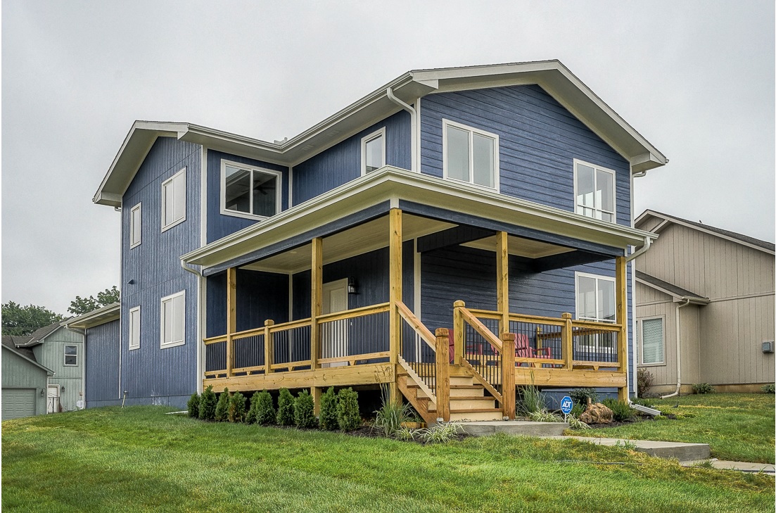 A Newly Built Blue House With A Large Wooden Porch